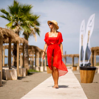 Pretty young woman in red dress walking on a beach at summer