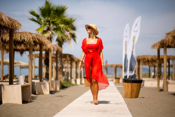 Pretty young woman in red dress walking on a beach at summer