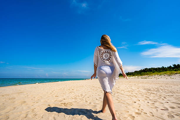 Beautiful middle aged woman walking on sandy beach in summertime. back view