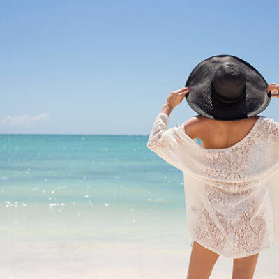 Woman in black summer hat on the beach standing with her back to the camera